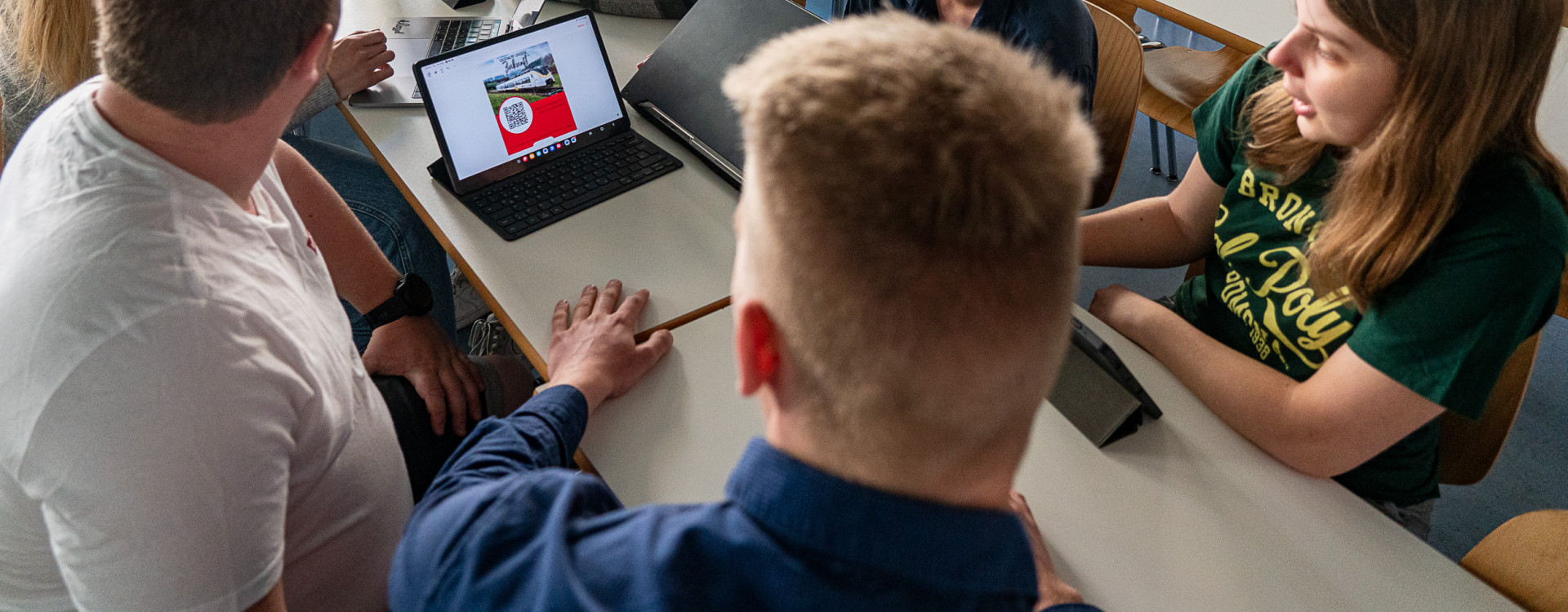 Sechs Studierende sitzen um einen Tisch mit geöffnetem Laptop