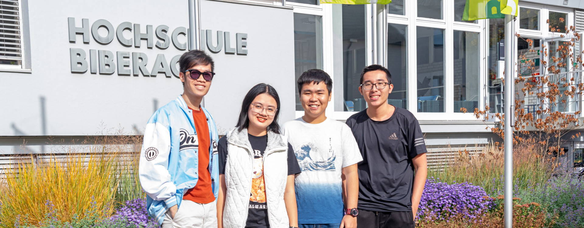 Studierende aus Vietnam stehend vor HBC-Schriftzug