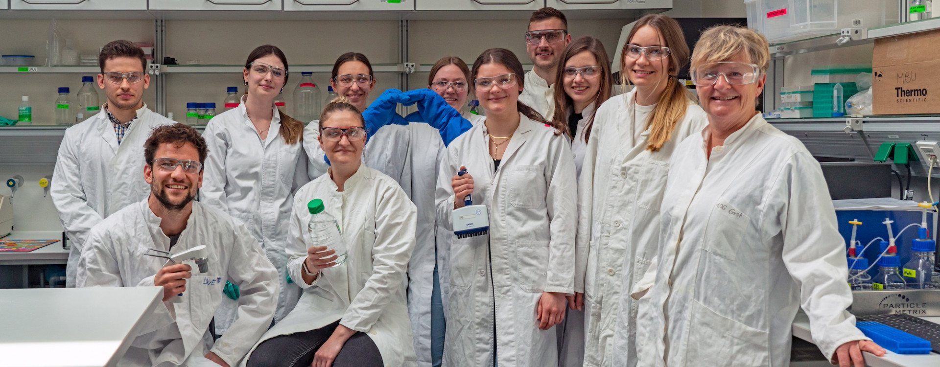 Gruppe von Menschen in Laborkitteln und mit Schutzbrillen