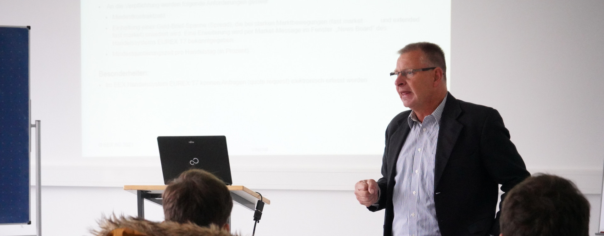 Mann steht vor Studierenden und hält Vortrag