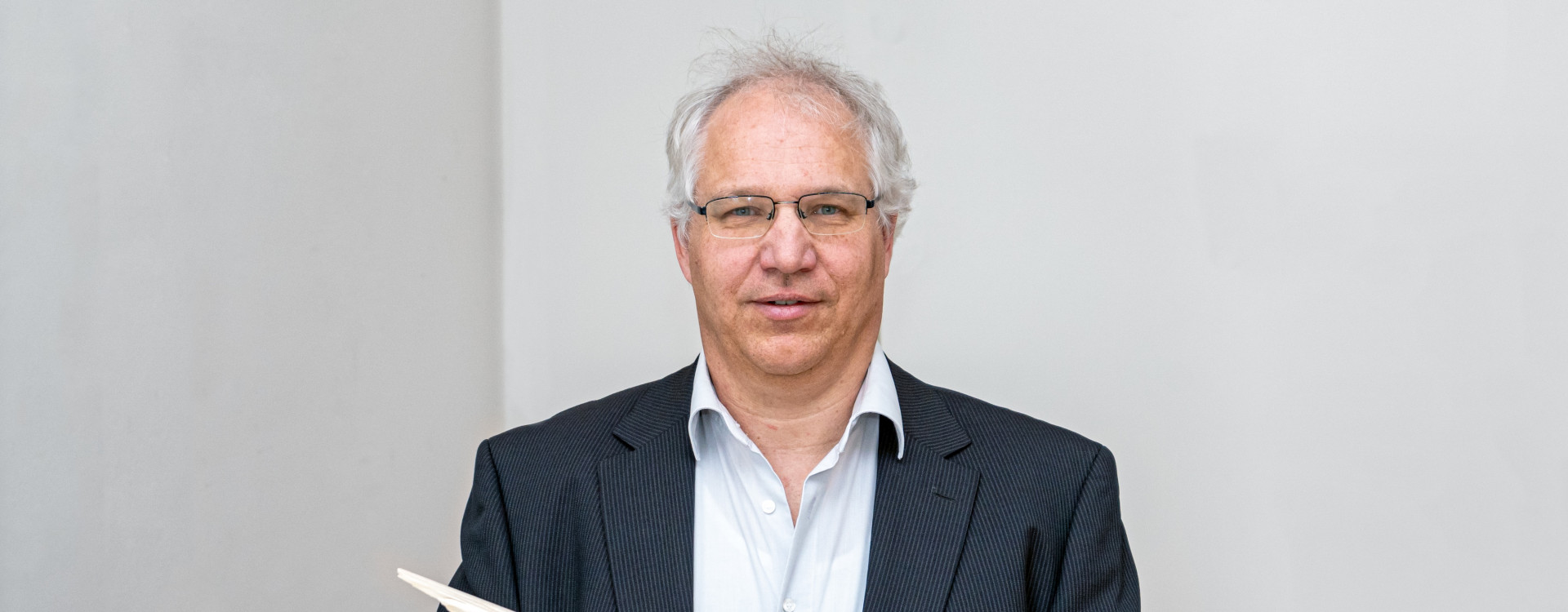 Mann im Anzug steht vor einer weißen Wand und hält Holz in der Hand