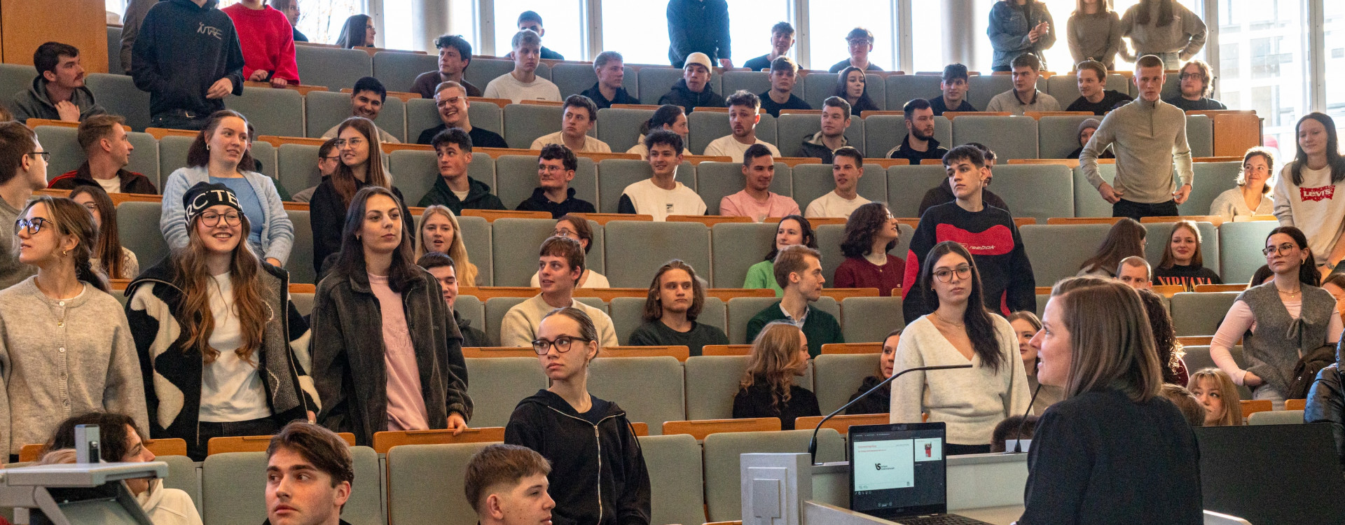 Studierende sitzen und stehen in einem Hörsaal