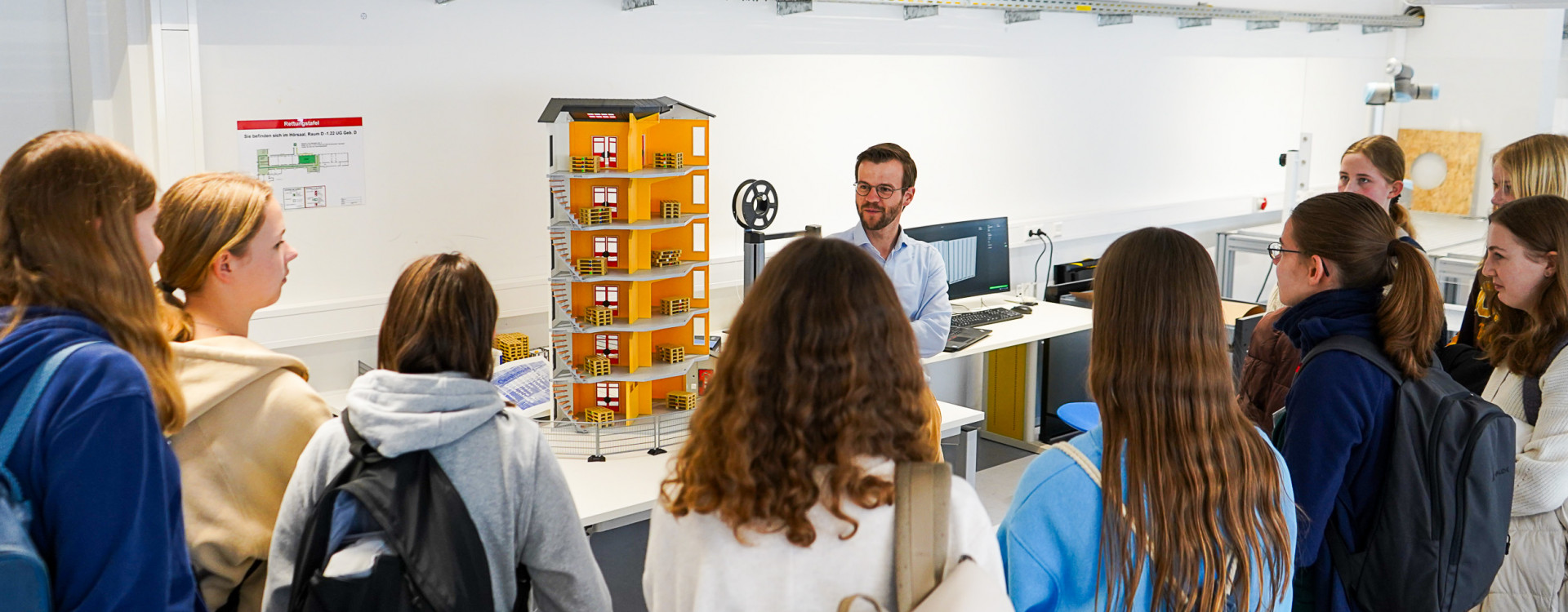 Schülerinnen stehen im Labor und hören Professor zu