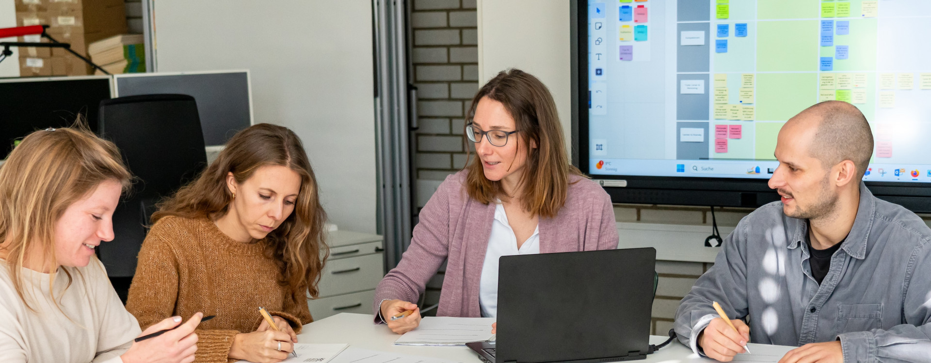 Drei Frauen und ein Mann sitzen an Tischen und arbeiten