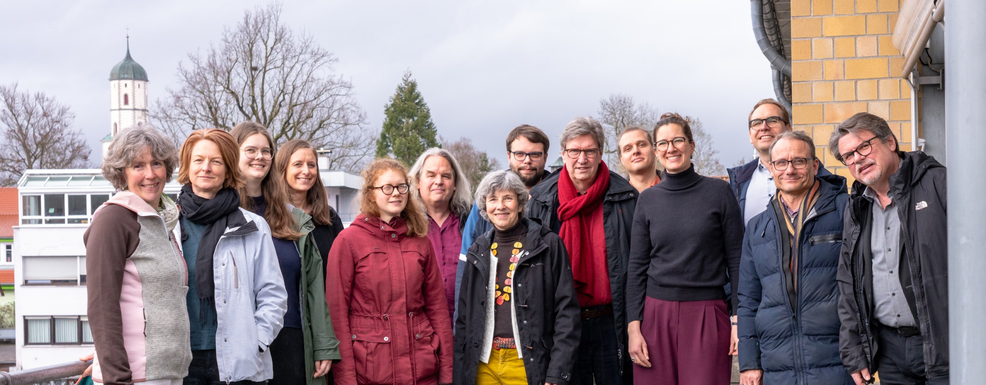 Viele Personen stehen draußen und lachen in die Kamera