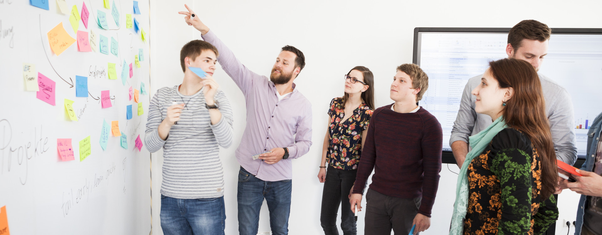 Gruppe von mehreren Menschen vor Whiteboard mit bunten Aufklebern