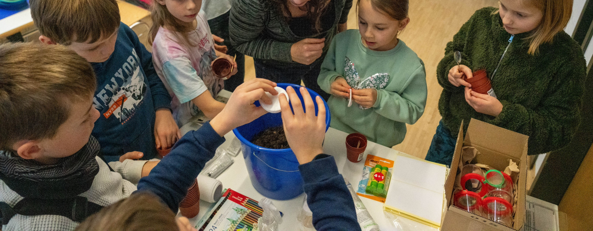 Kinder stehen mit Dozentin um Tisch und erforschen Boden