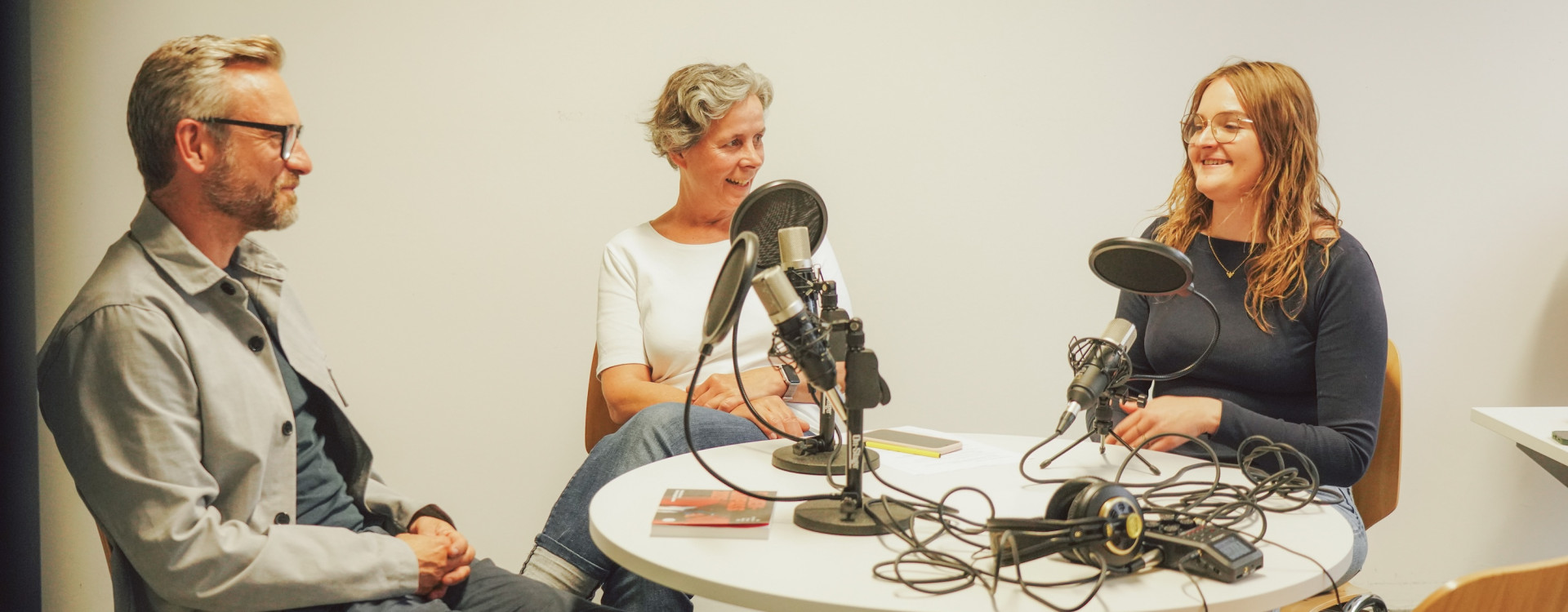 Drei Personen sitzen an einem runden Tisch bei einer Podcastaufnahme