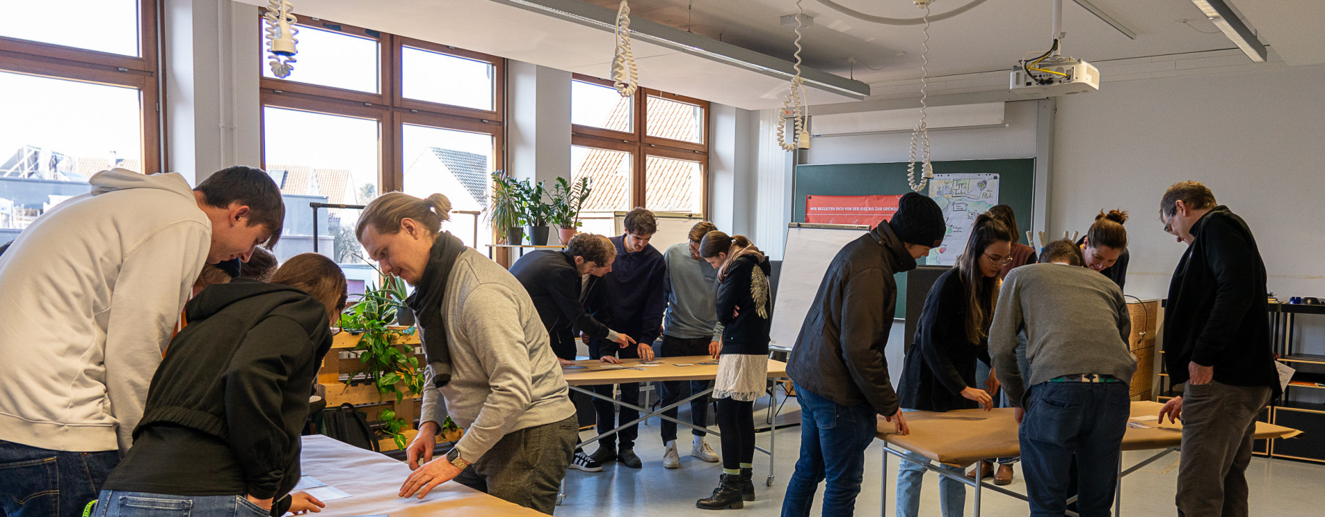 Personen stehen um drei Tische herum und arbeiten interaktiv