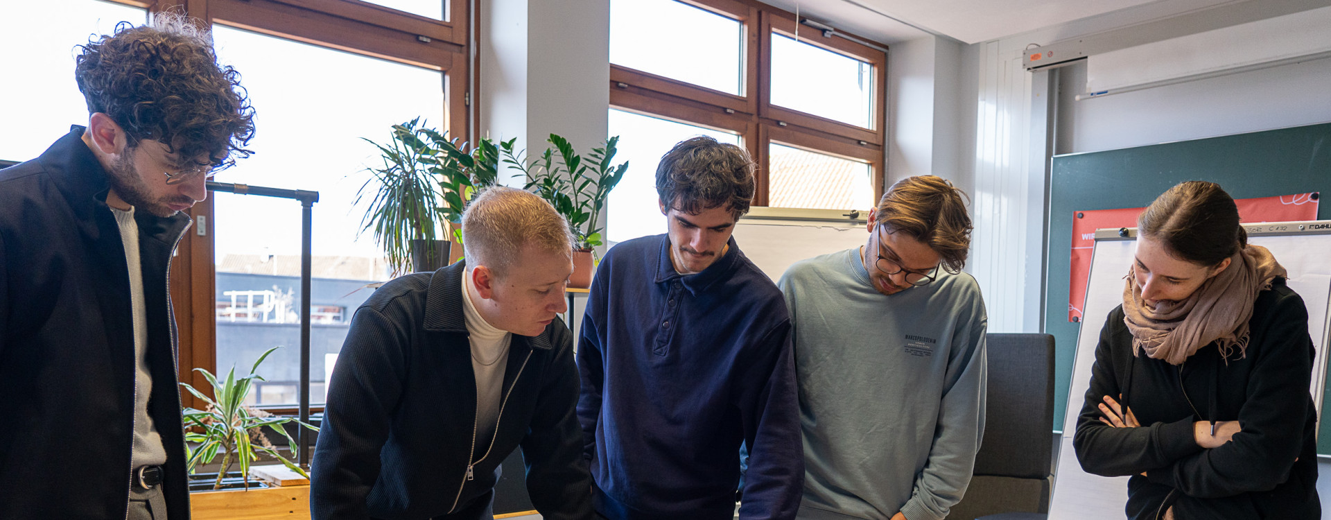 Personen stehen um einen Tisch herum und arbeiten interaktiv