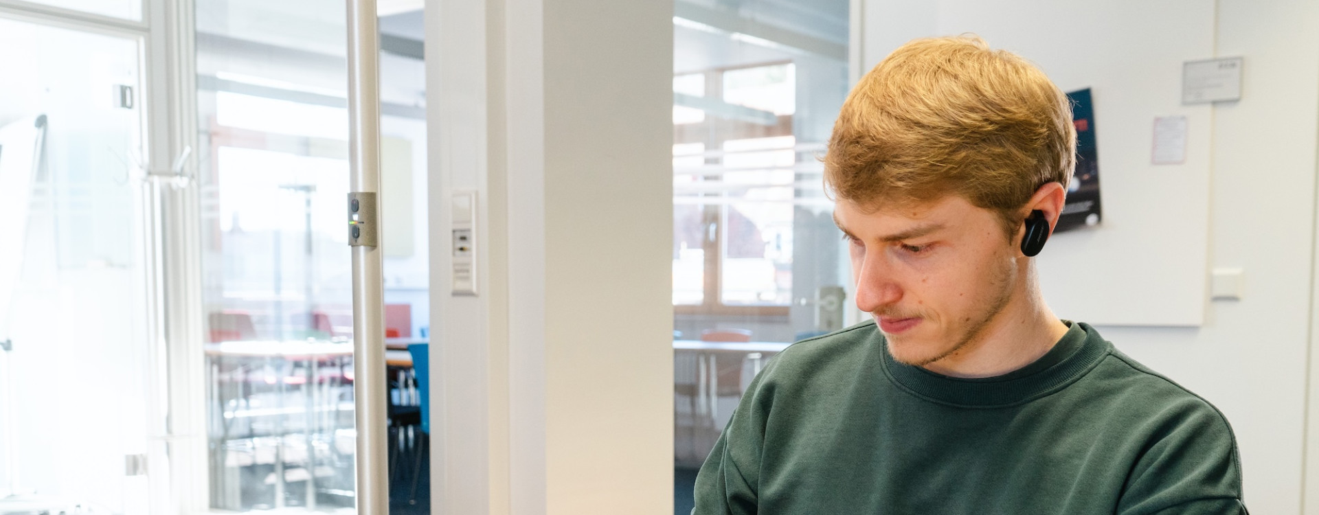 Ein junger Mann sitzt an einem Tisch und arbeitet am Laptop und Handy