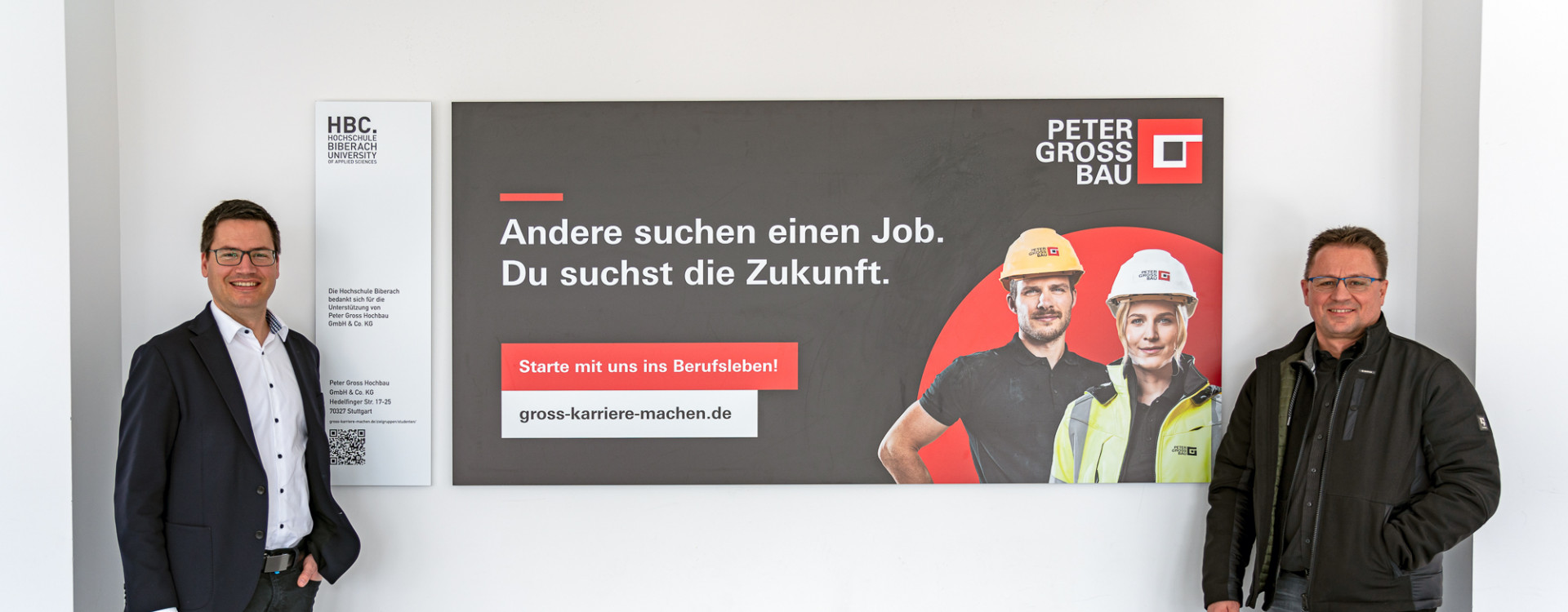 Zwei Männer stehen links und rechts neben einem großen Banner von Peter Groß Bau