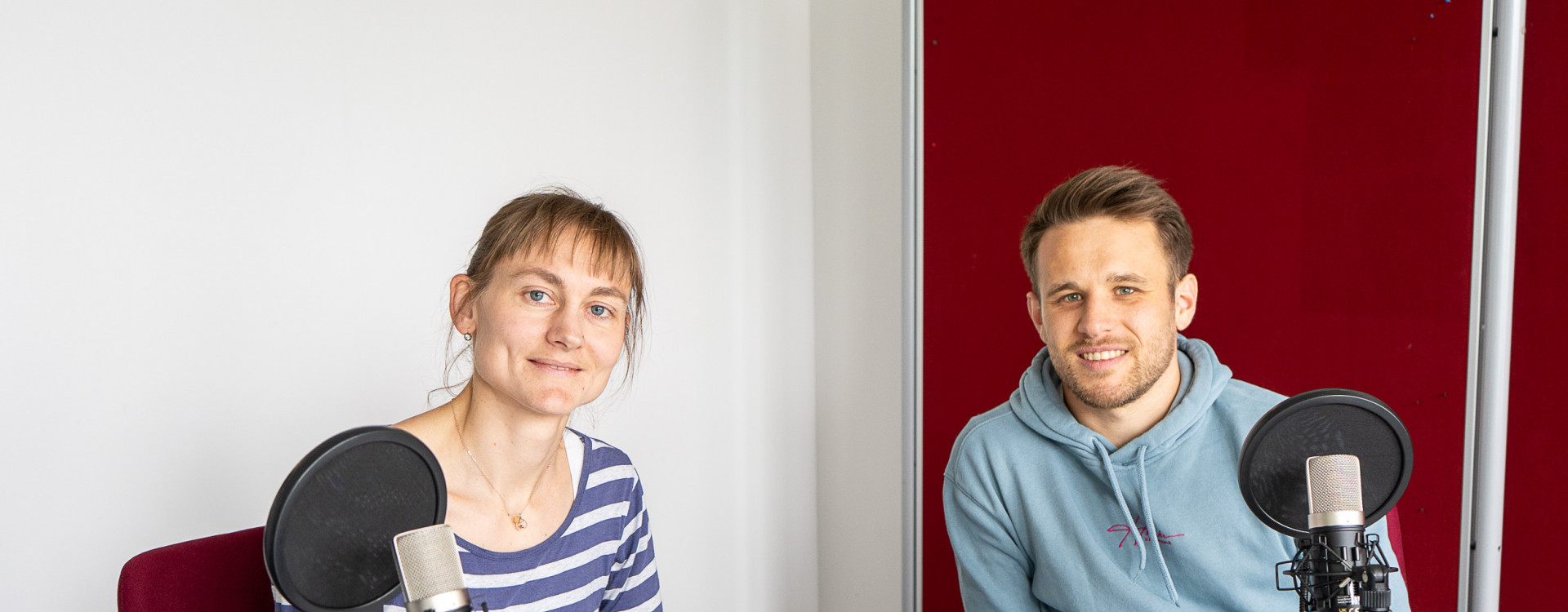 Eine Frau und ein Mann sitzen an einem Tisch und nehmen einen Podcast auf