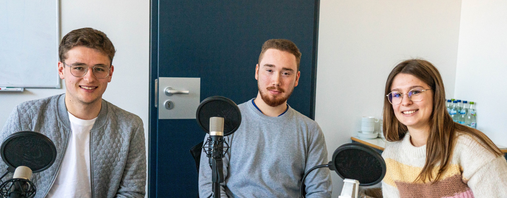 Drei Studierende sitzen mit Mikrofonen um einen Tisch