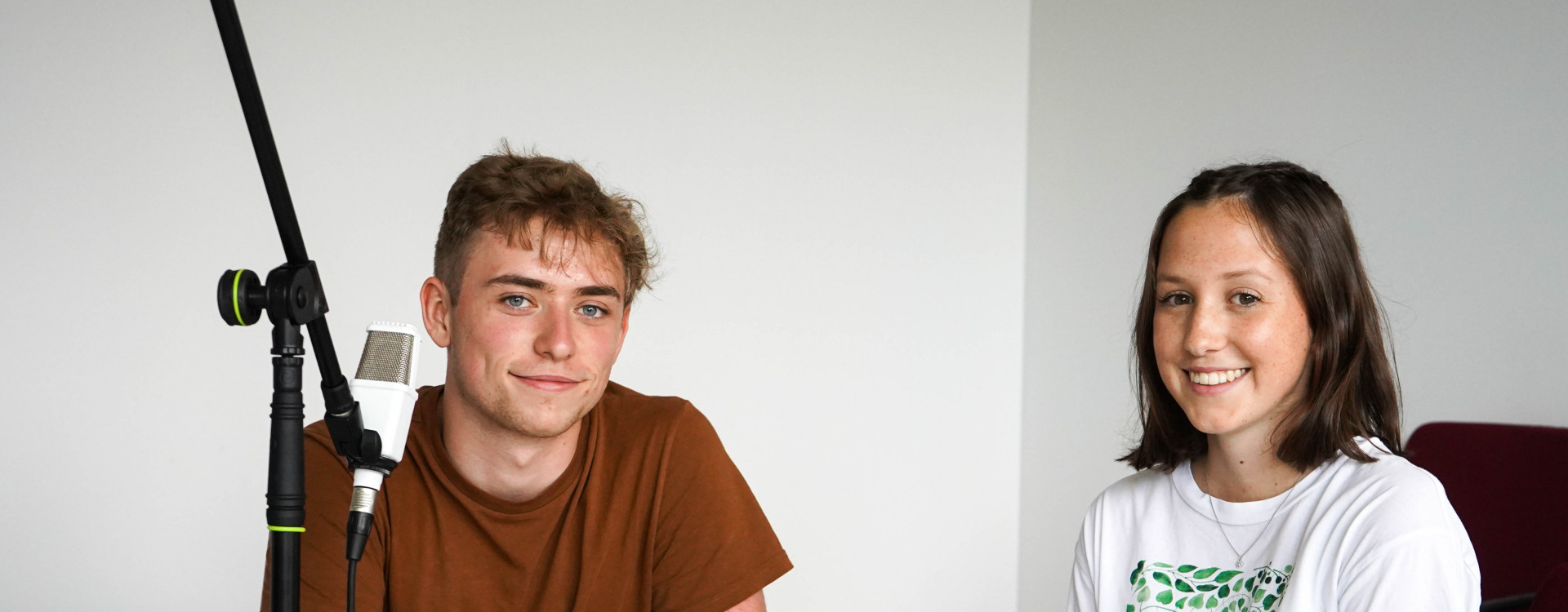 Ein Mann und eine Frau sitzend am Tisch bei einer Podcast-Aufnahme.