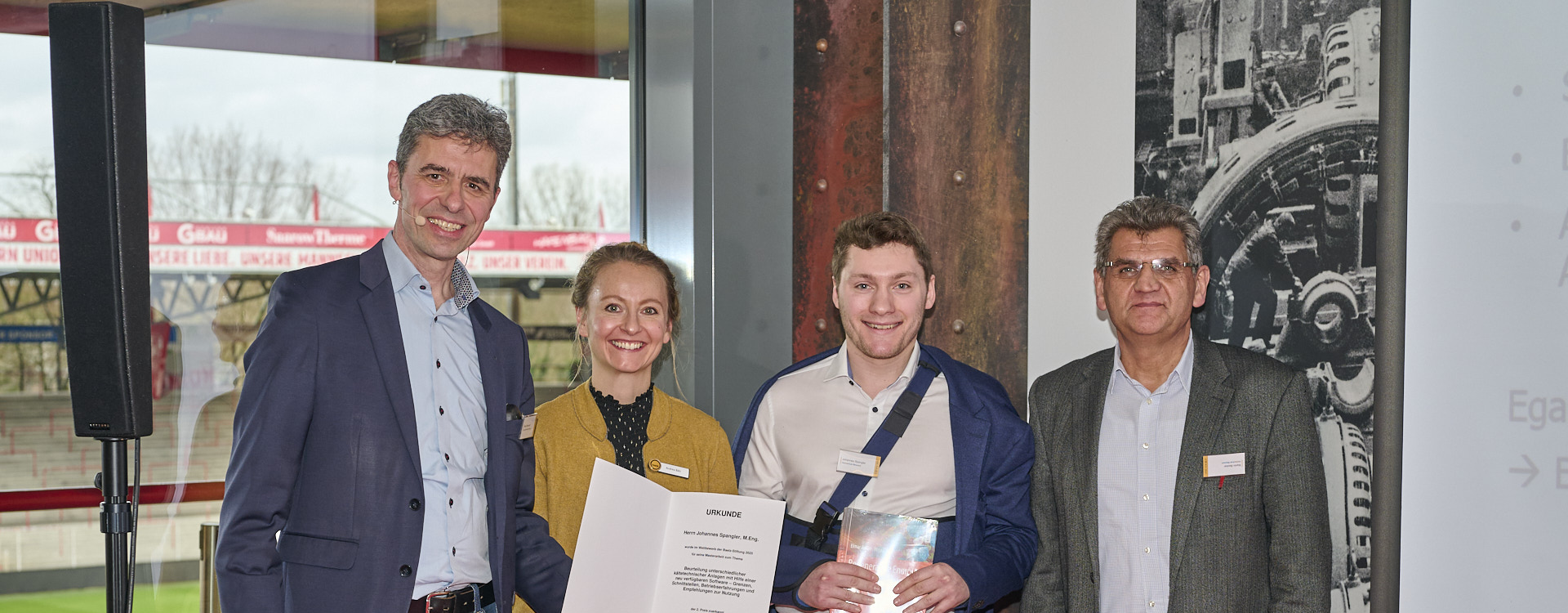 Vier Personen stehen lachend mit einer Urkunde