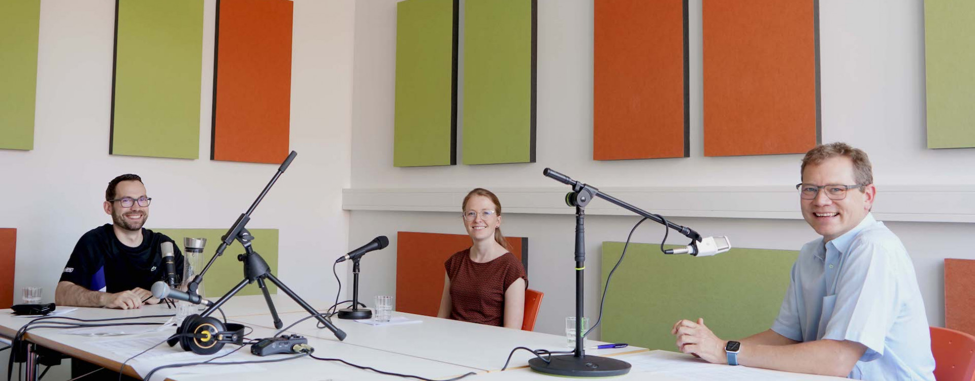 Drei Personen bei Podcastaufnahme an einem Tisch