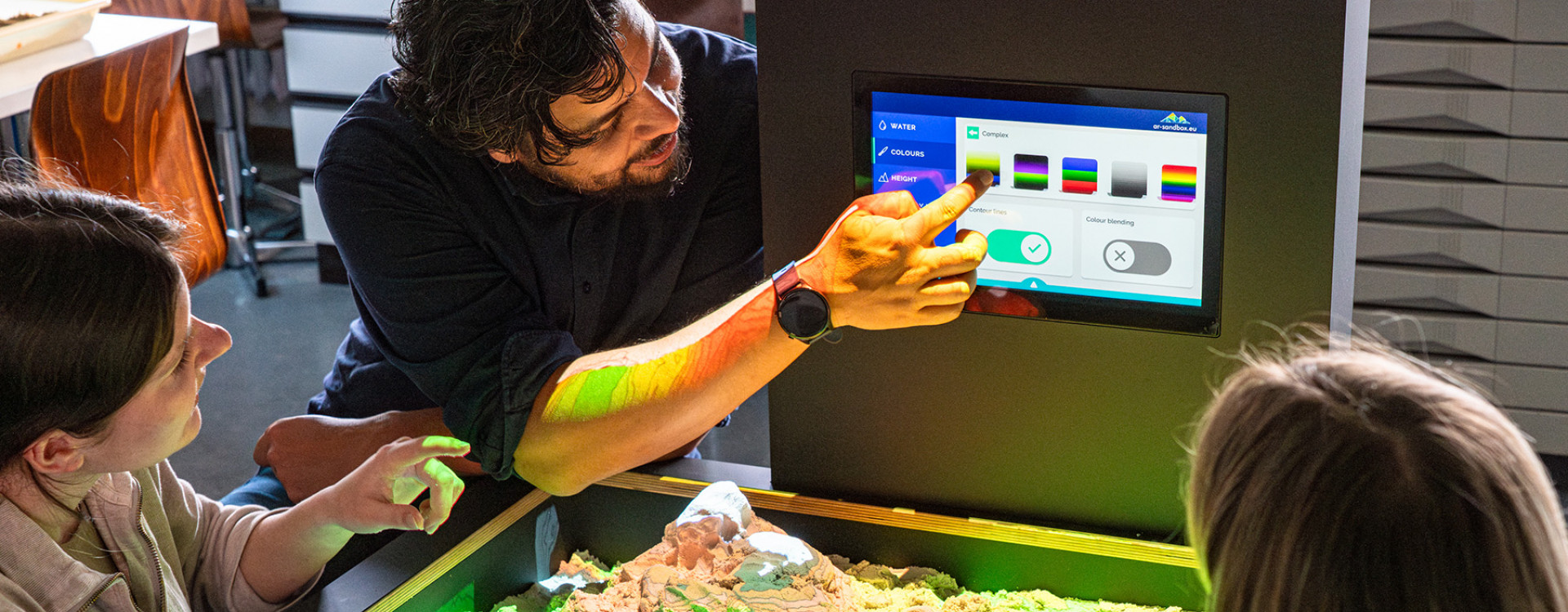 Professor Julius Jara gemeinsam mit zwei Studierenden an der AR-Sandbox