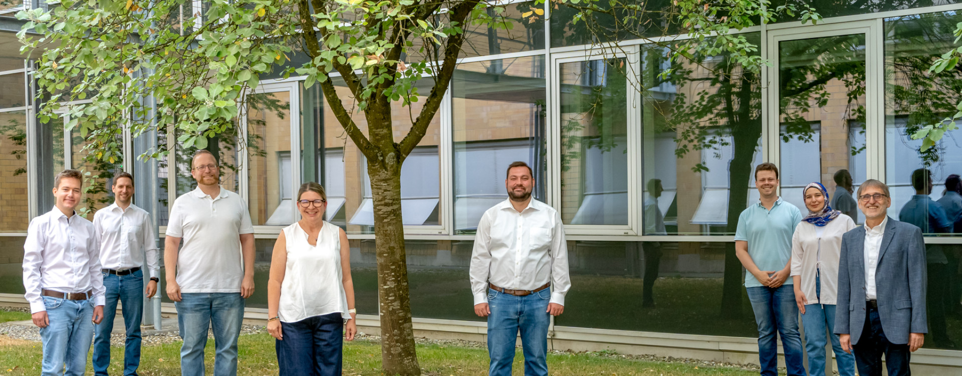 8 Mitarbeiter*innen stehen auf einer grünen Wiese