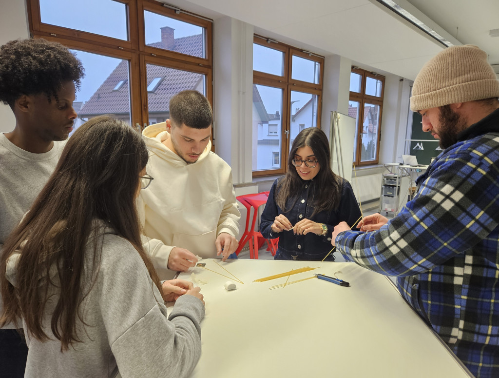 Studierende stehen an einem Tisch und basteln mit Marshmallows