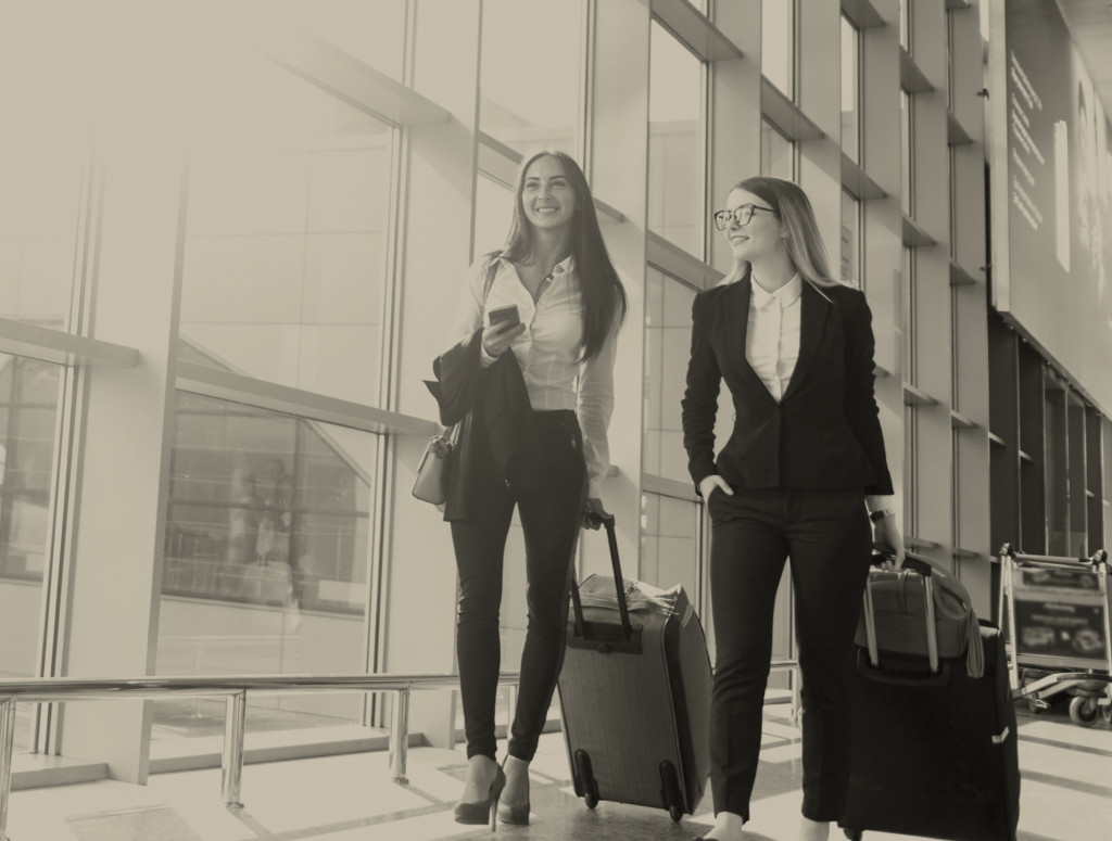 Zwei Frauen ziehen zwei Koffer hinter sich her. Business Trip