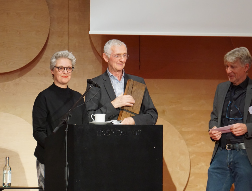 Drei Personen vor Stehpult auf einer Bühne