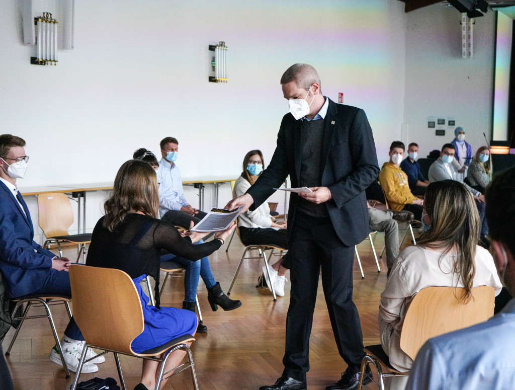 Mann übergibt Urkunde an Frau in einem Stuhlkreis.