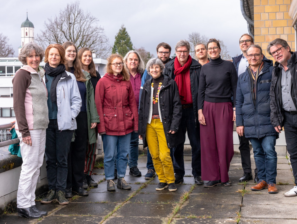 Viele Personen stehen draußen und lachen in die Kamera