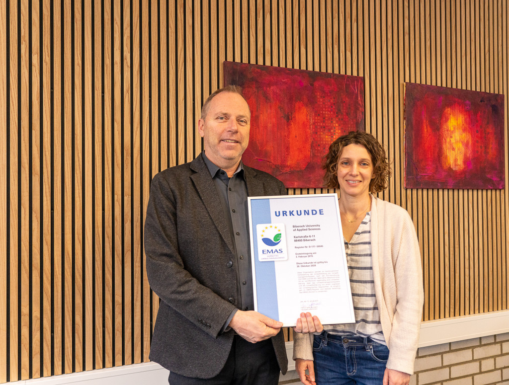 Ein Mann und eine Frau halte eine Urkunde von EMAS in die Kamera
