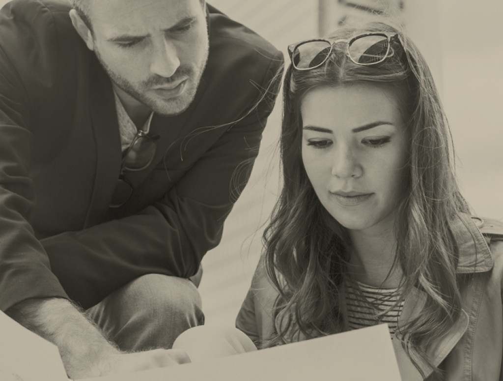 Eine Frau und ein Mann sitzen vor Bauplänen, schwarz weiß