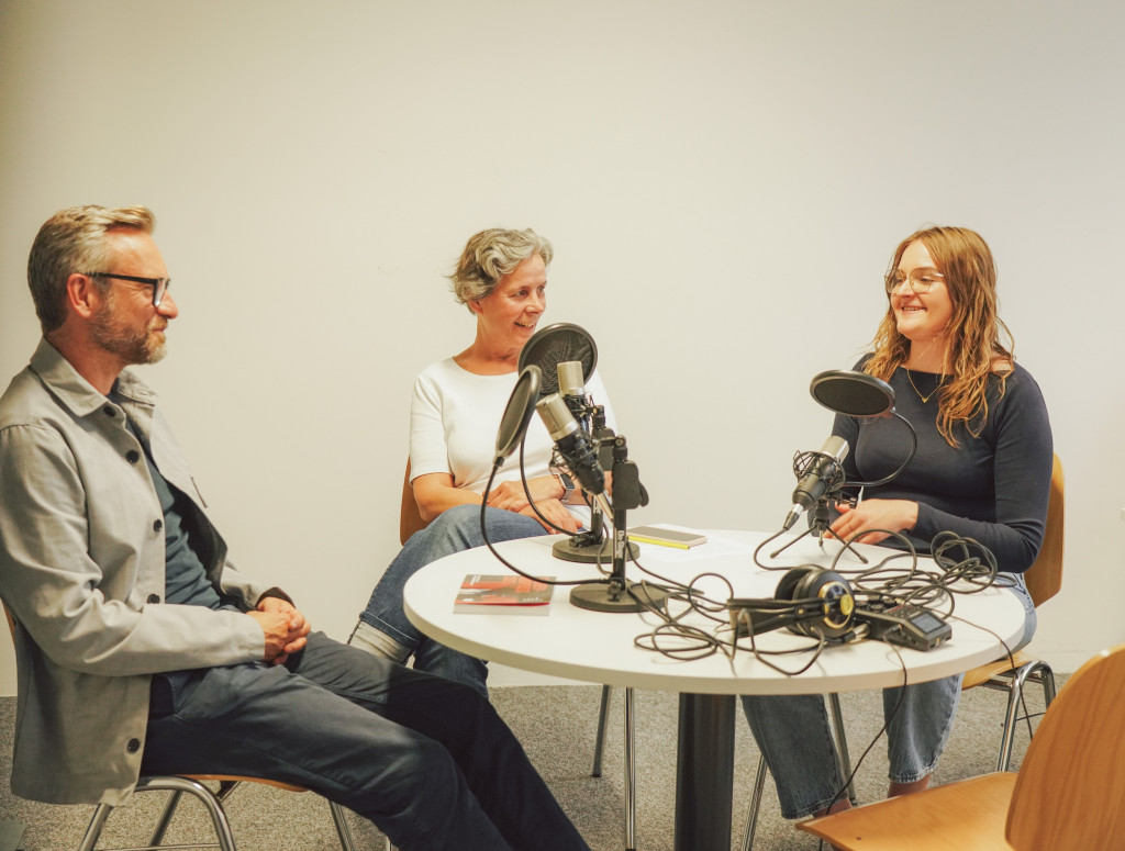 Drei Personen sitzen an einem runden Tisch bei einer Podcastaufnahme