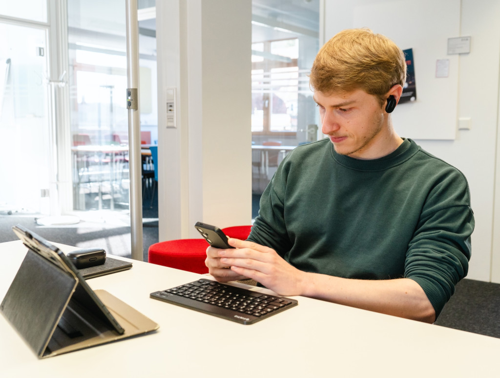 Ein junger Mann sitzt an einem Tisch und arbeitet am Laptop und Handy