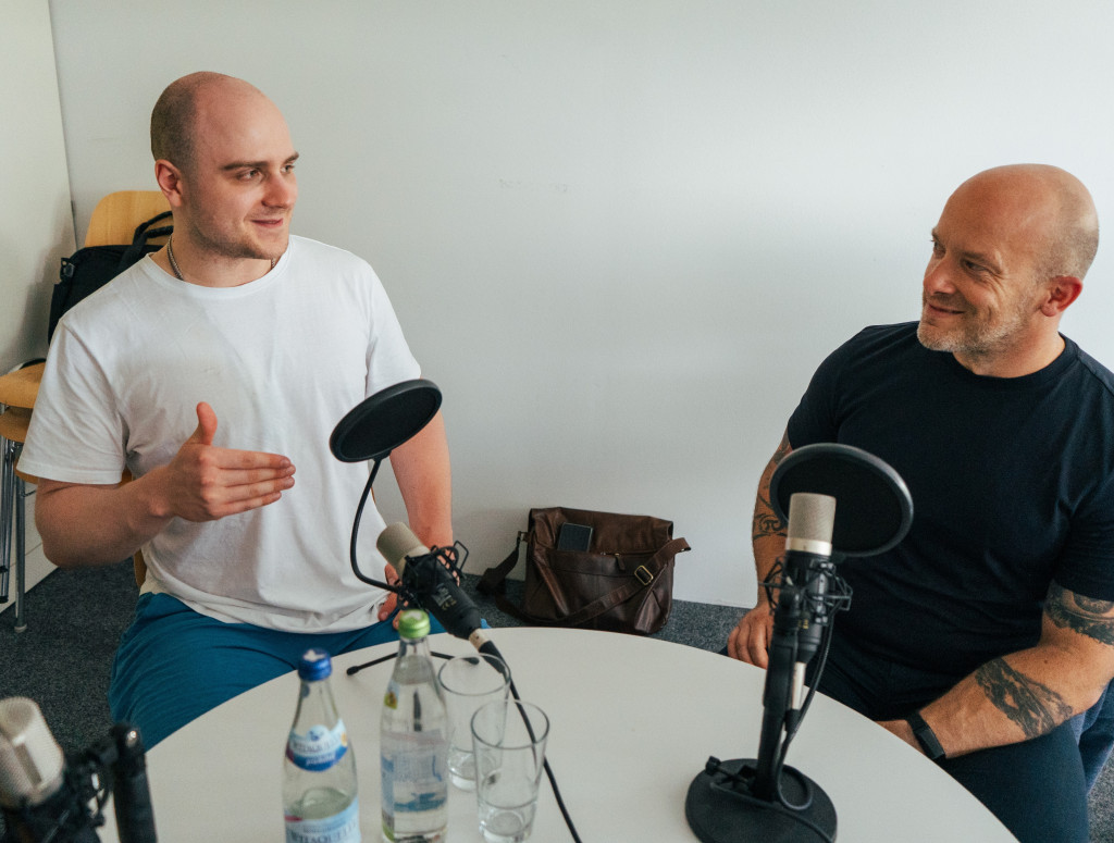 Zwei Männer sitzen an einem Tisch bei einer Podcastaufnahme