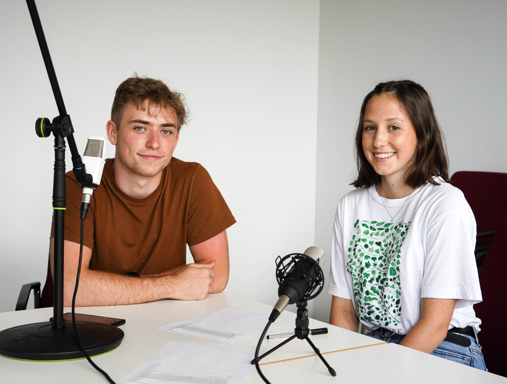 Ein Mann und eine Frau sitzend am Tisch bei einer Podcast-Aufnahme.