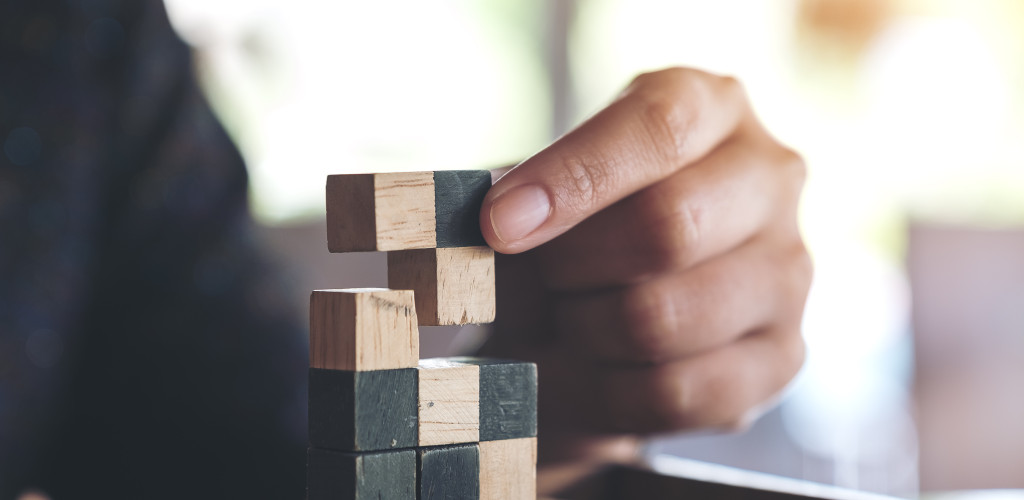 Eine Hand setzt Tetrisbausteine übereinander