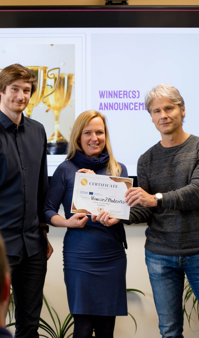 Ein Mann übergibt Urkunde an eine Frau und einen Mann