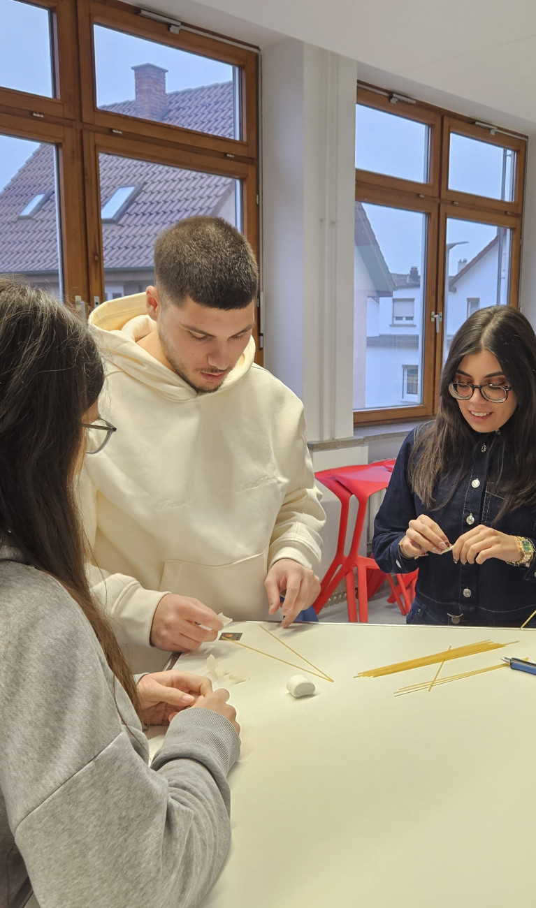Studierende stehen an einem Tisch und basteln mit Marshmallows