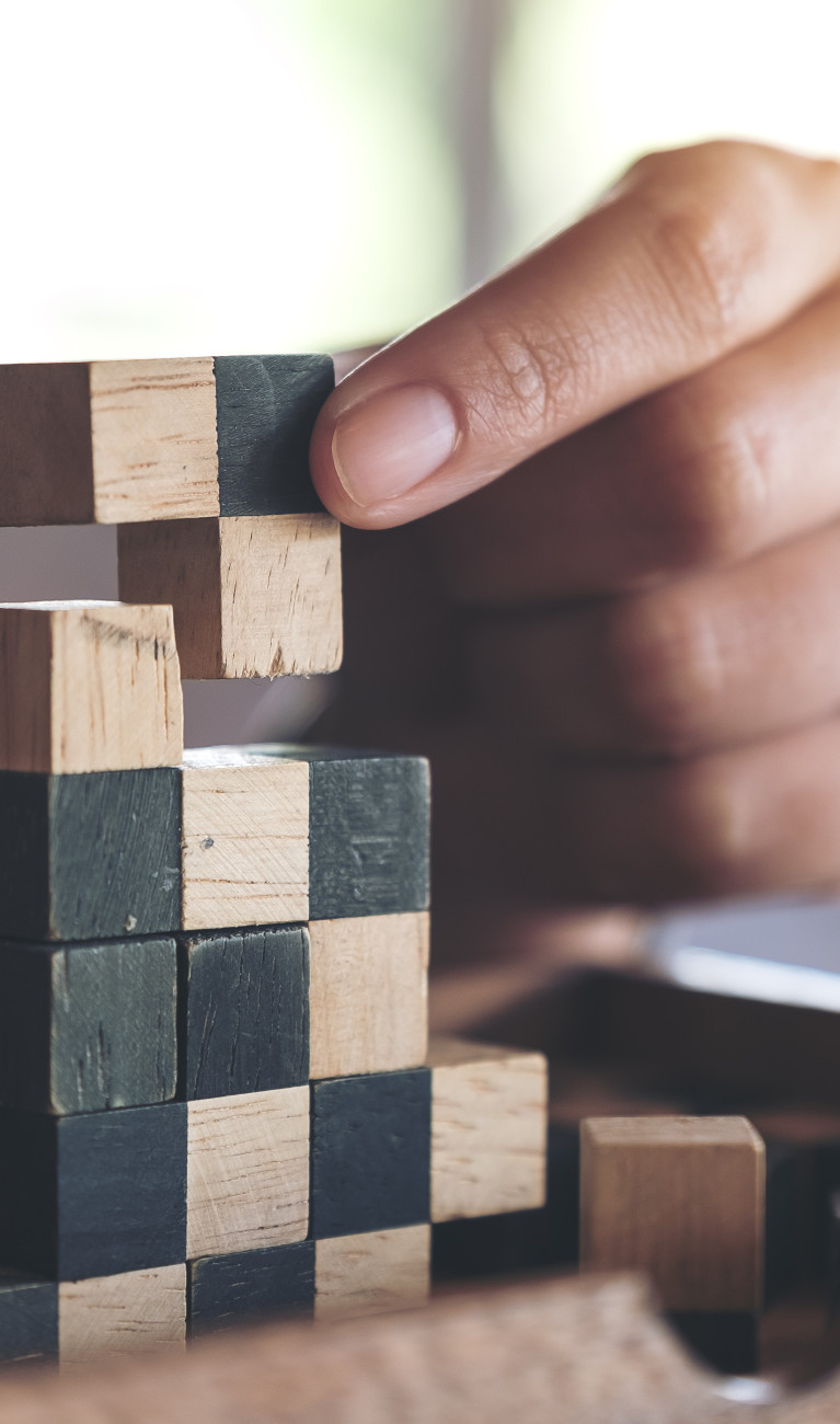 Eine Hand setzt Tetrisbausteine übereinander 