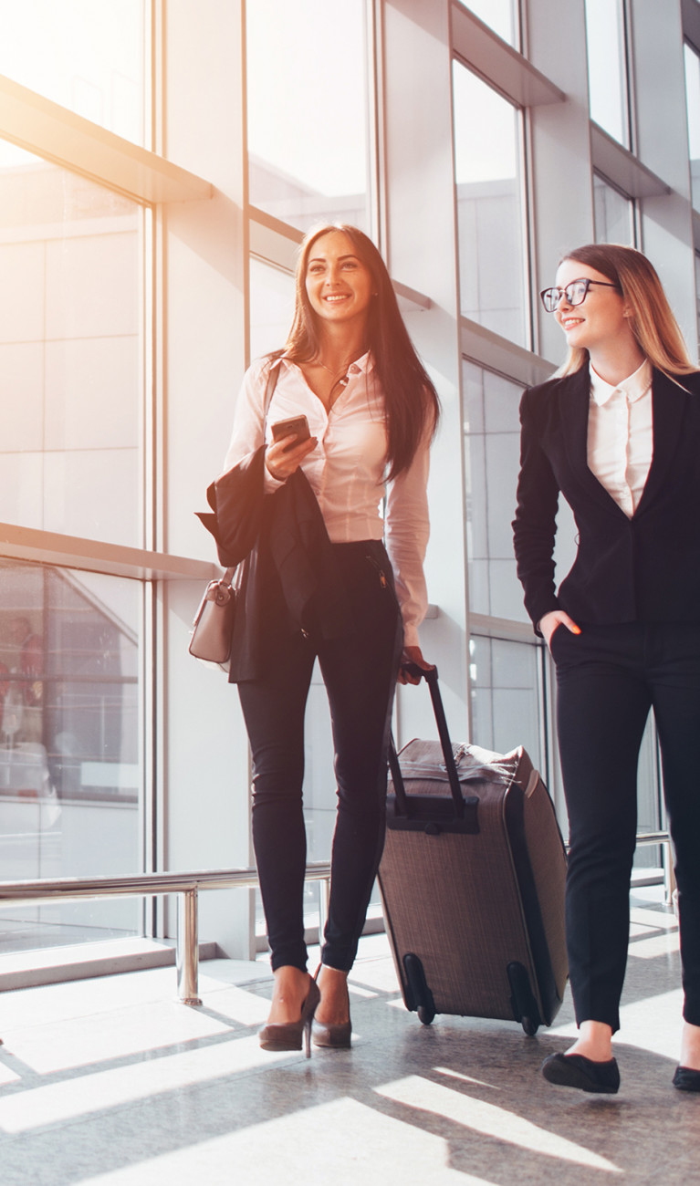 Zwei Frauen ziehen einen Koffer, sie sind auf einer Businessreise 