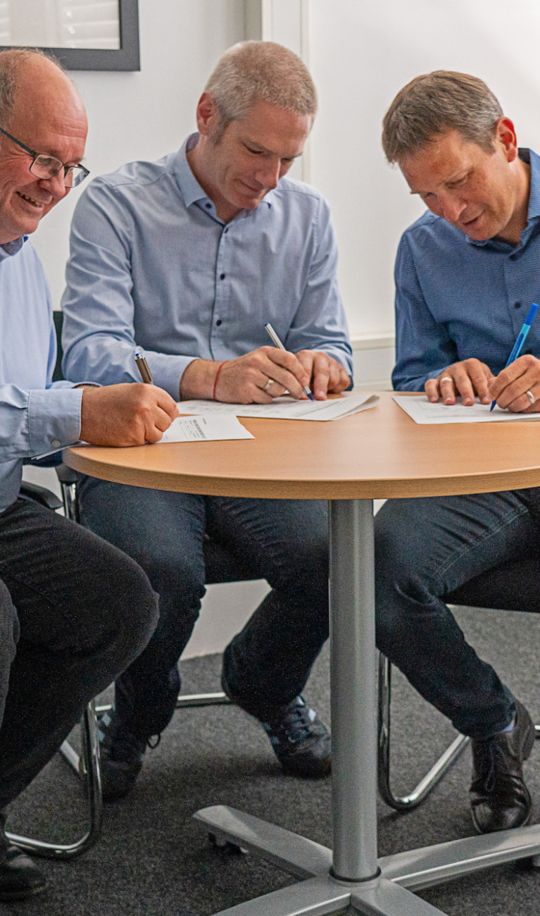 drei Männer unterzeichnen Vertrag an Tisch