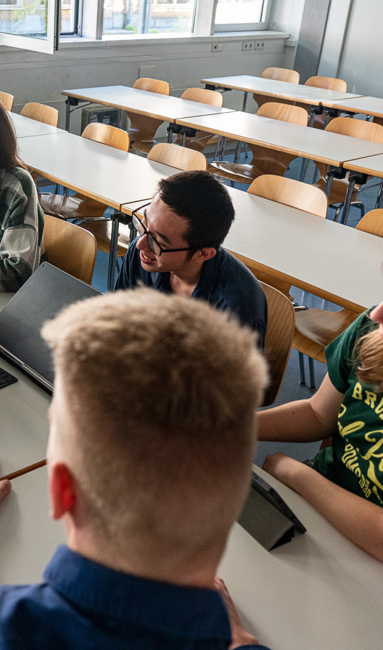 Sechs Studierende sitzen um einen Tisch mit geöffnetem Laptop