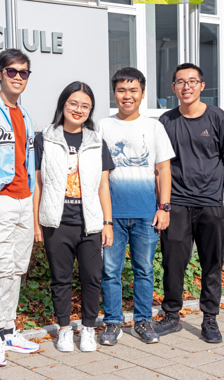 Studierende aus Vietnam stehend vor HBC-Schriftzug