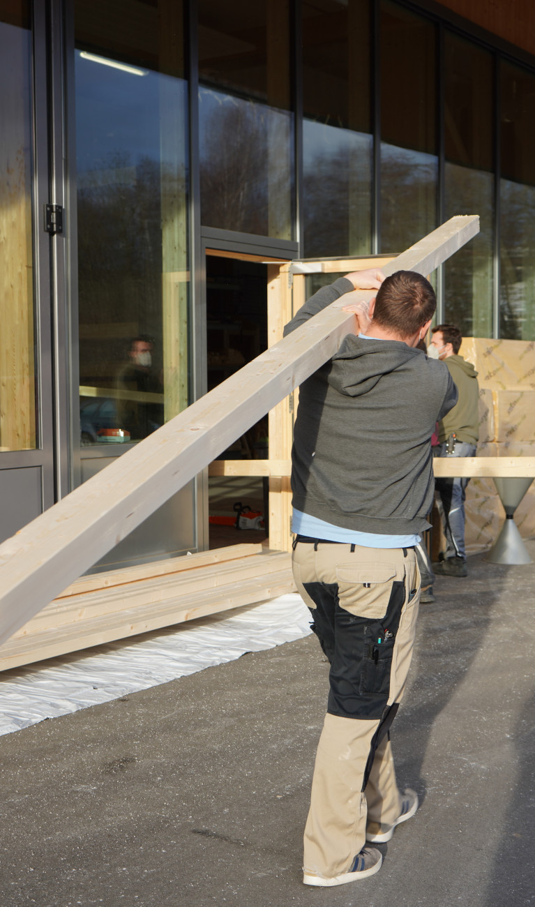 Studierender trägt Holzbalken über der Schulter