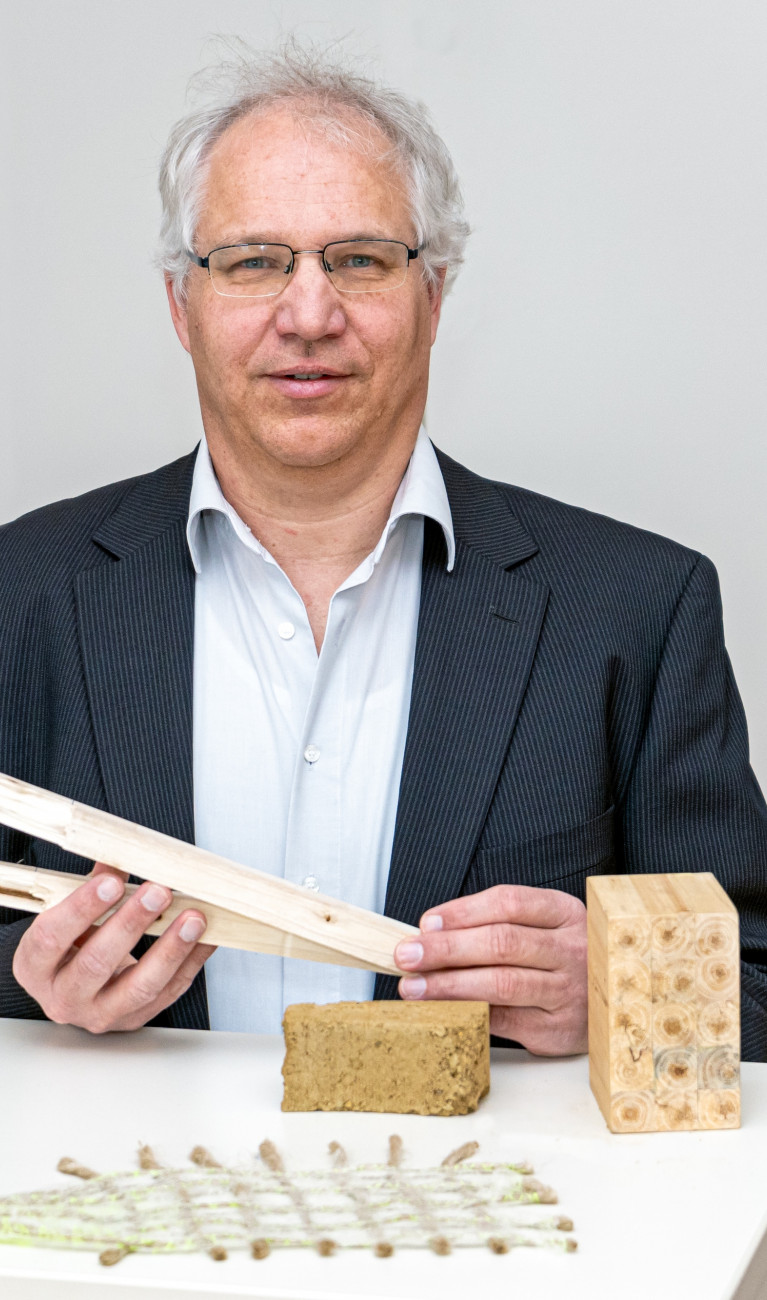 Mann im Anzug steht vor einer weißen Wand und hält Holz in der Hand