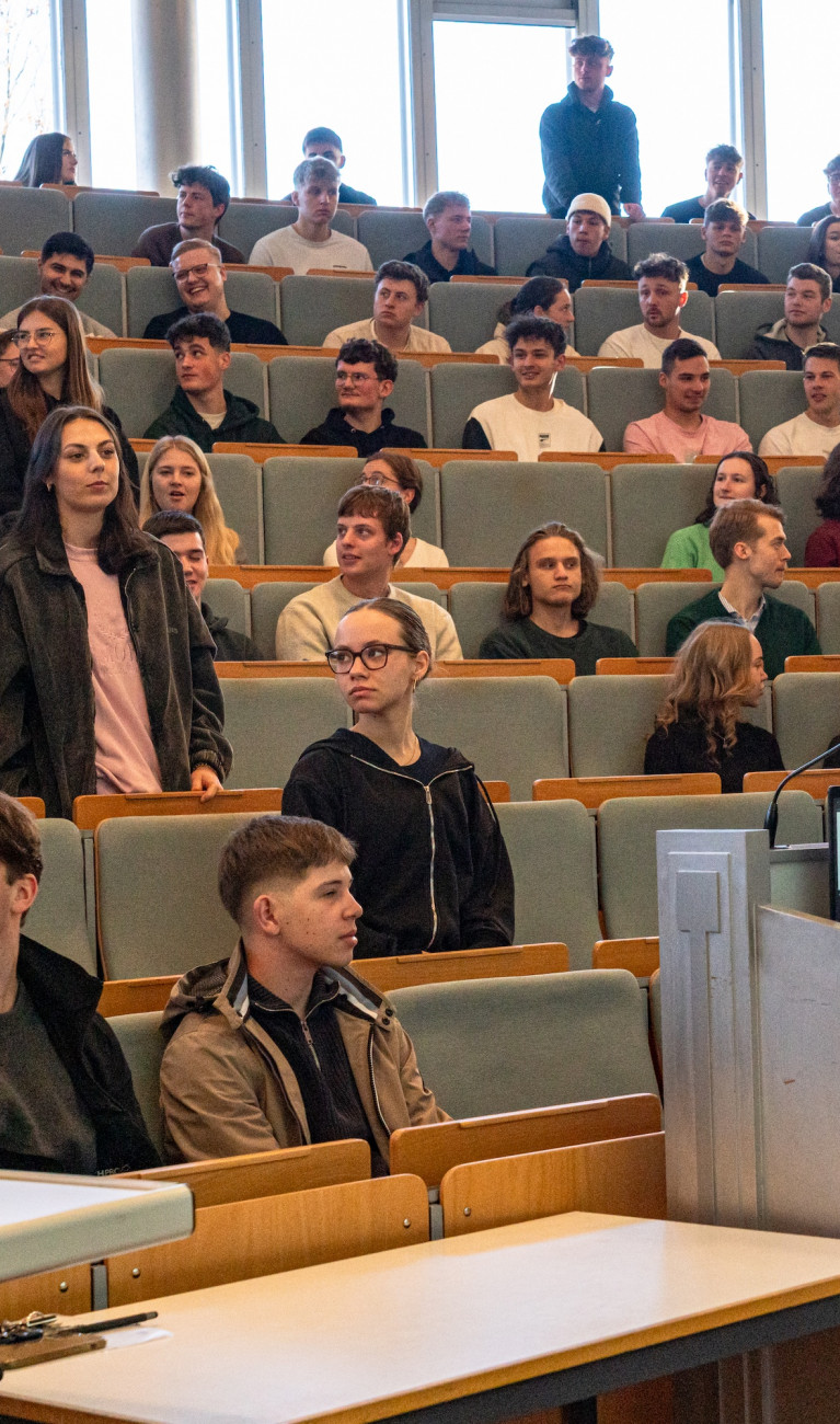 Studierende sitzen und stehen in einem Hörsaal