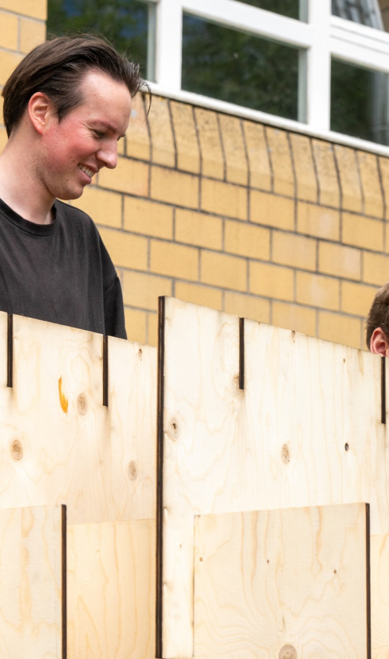 Zwei Studierende bauen ein Pavillon aus Holz auf 