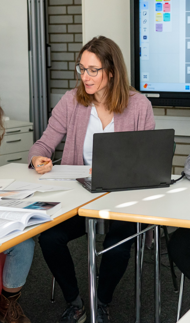 Drei Frauen und ein Mann sitzen an Tischen und arbeiten