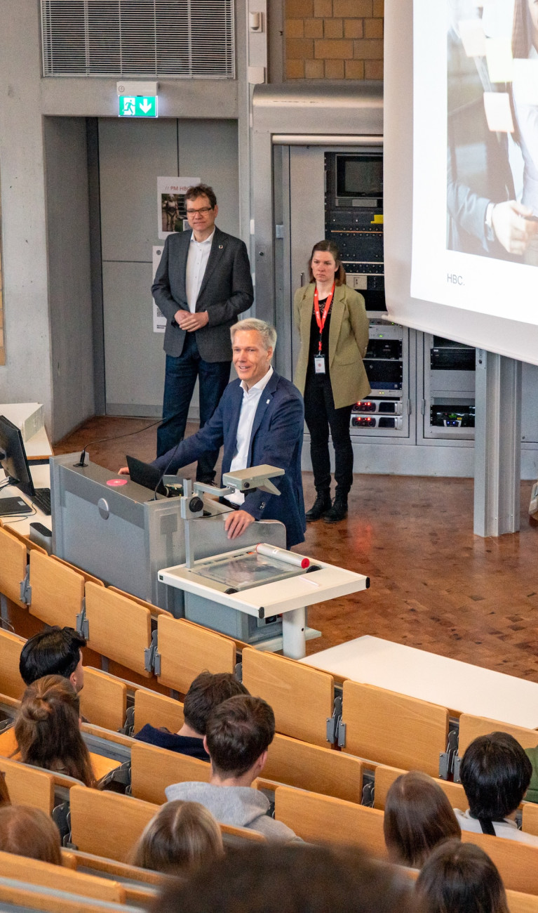 Prof. Bahr steht im Hörsaal und begrüßt Studierende