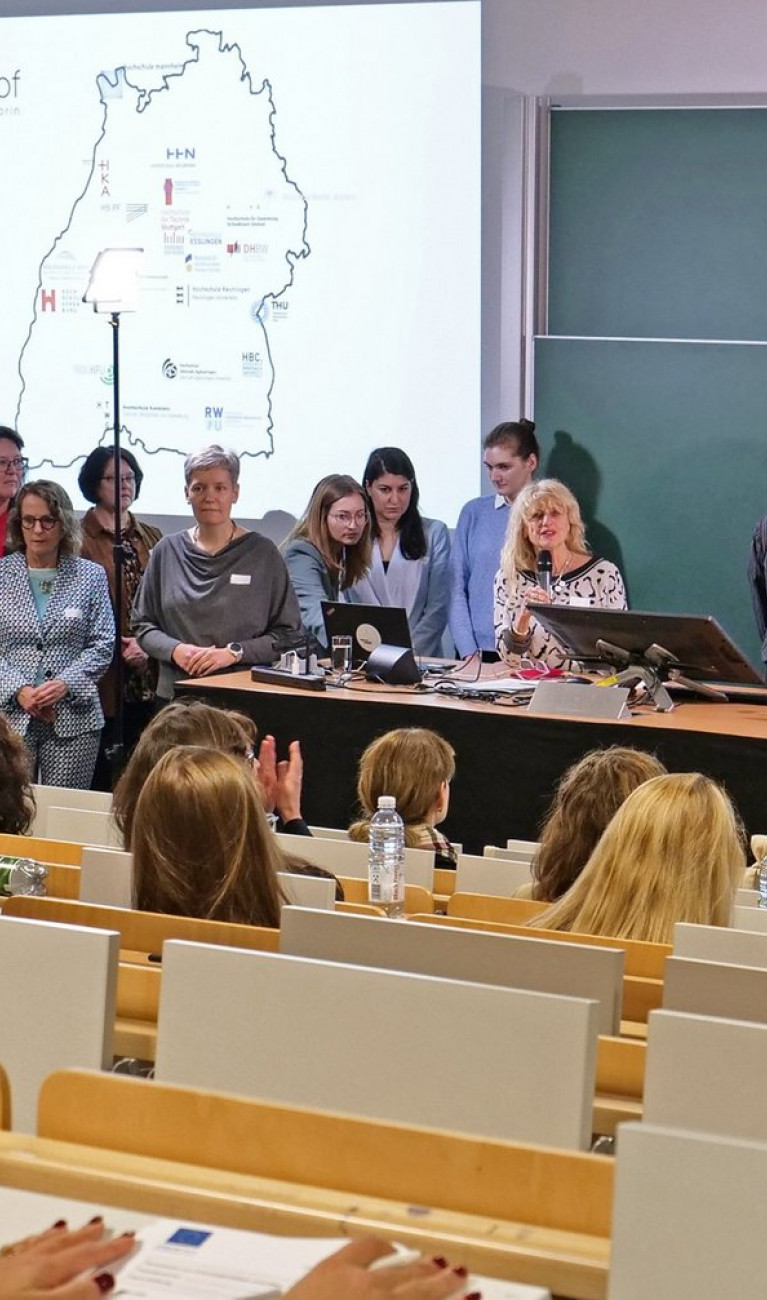 Viele Menschen stehen in Hörsaal vor Tafel