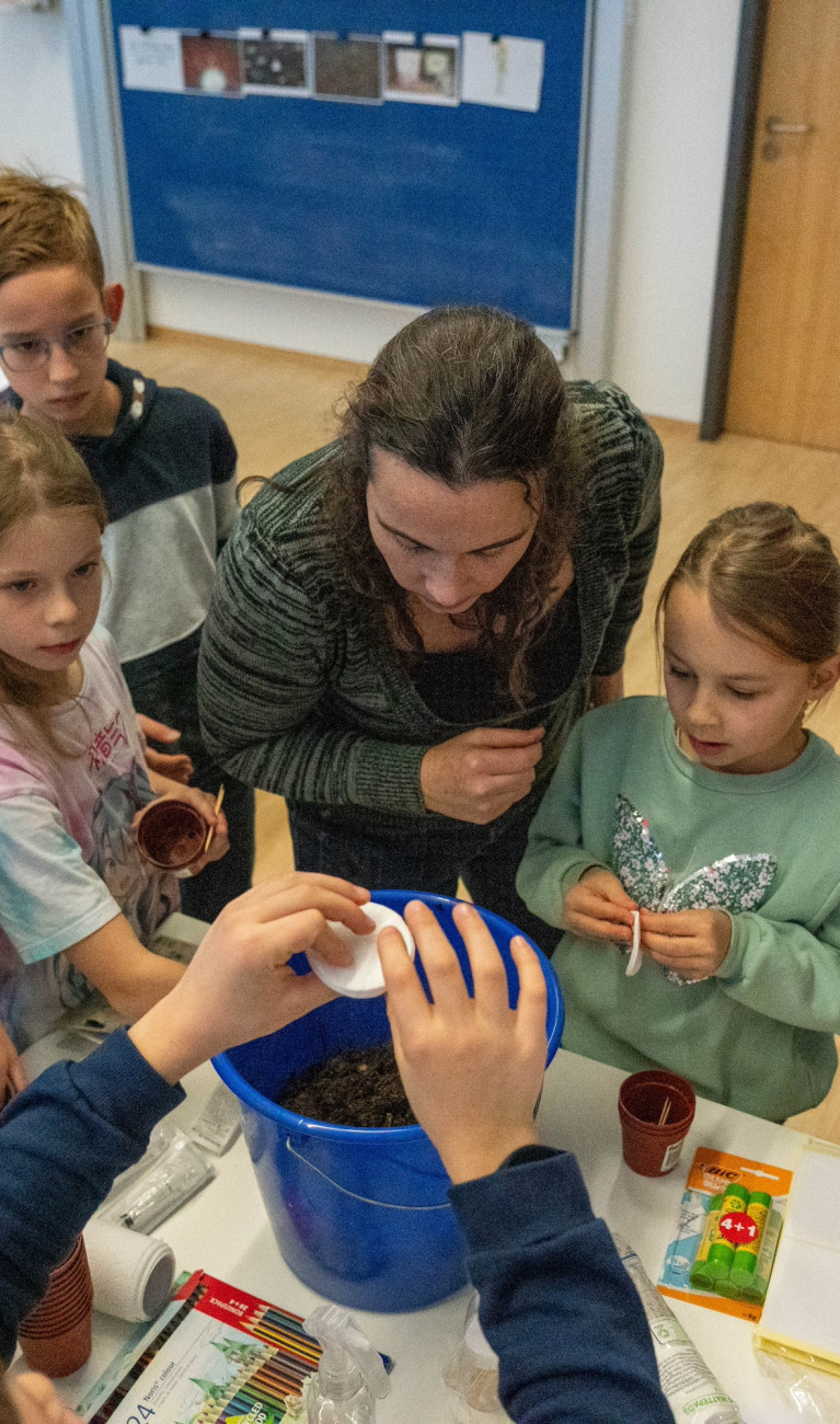 Kinder stehen mit Dozentin um Tisch und erforschen Boden